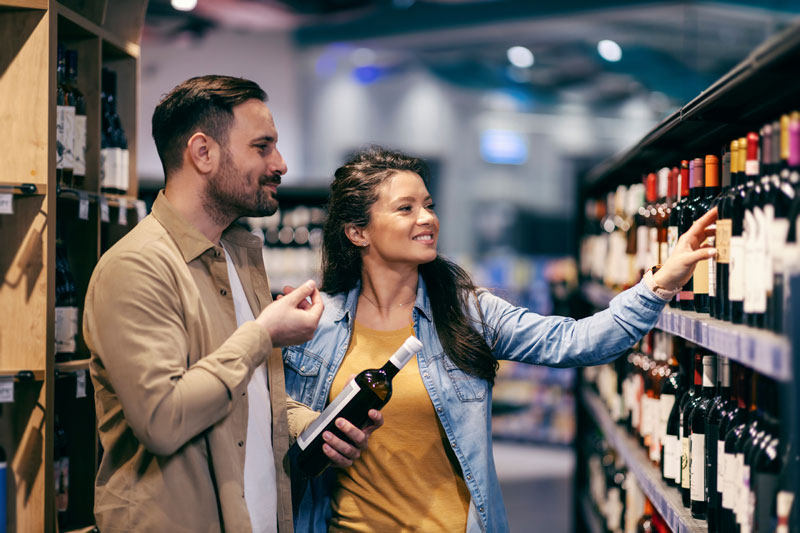 Happy Couple Choosing Good Wine At Supermarket For Dinner.
